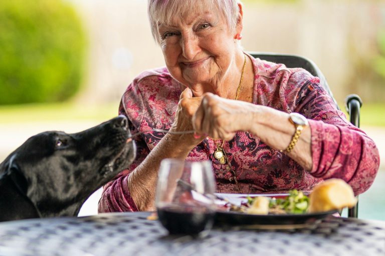 I miss you Mom An elderly woman smiles at a dog next to her while dining outdoors.